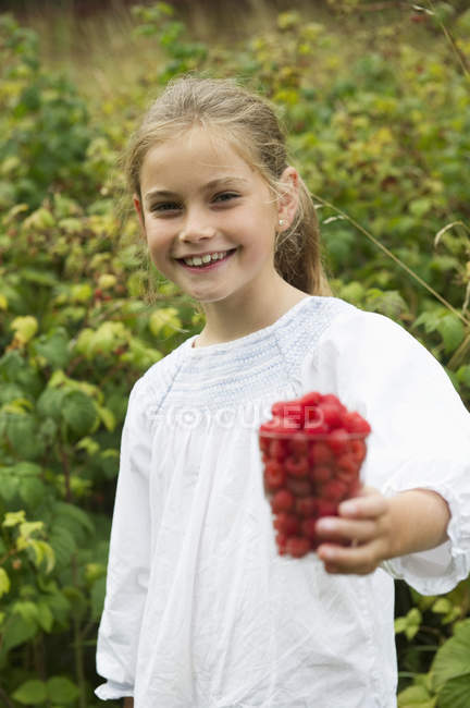 Girl with cup of raspberries looking at camera — Stock Photo