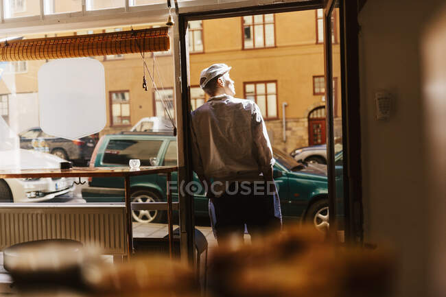 Visão traseira do açougueiro inclinado na porta da loja — Fotografia de Stock