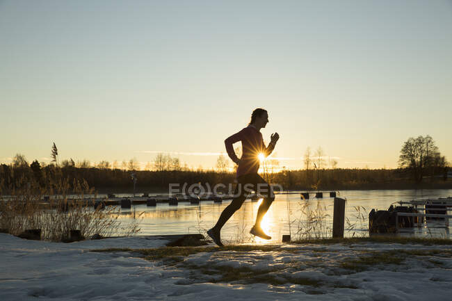 Silhueta de mulher jogging pelo lago ao pôr do sol — Fotografia de Stock