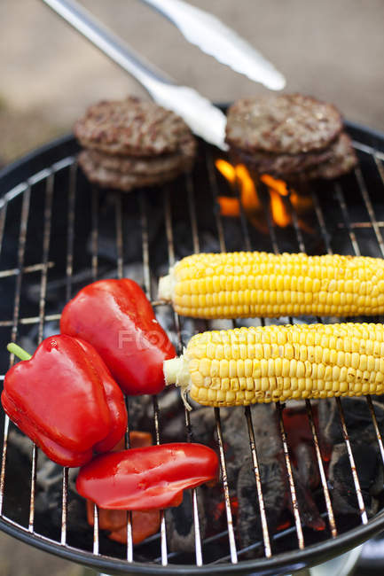 Hamburgers, corn and bell peppers on barbecue, focus on foreground — Stock Photo