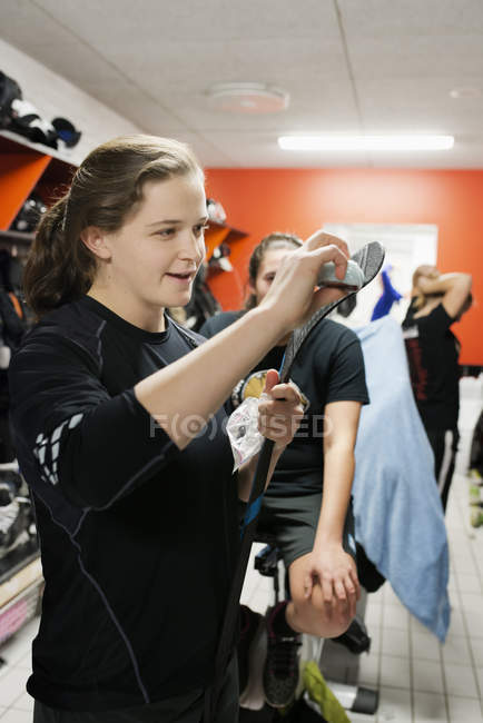 Young woman waxing hockey stick in locker room — Stock Photo