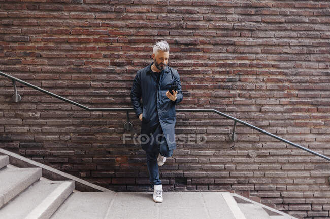 Человек у стены с брикетом на смартфоне — стоковое фото
