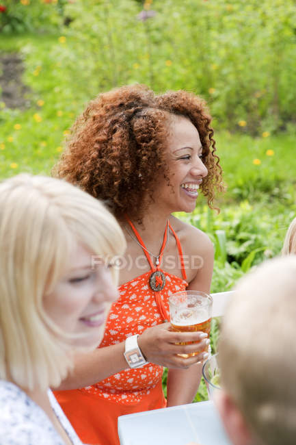 Woman with curly hair sitting at picnic table with glass of beer — Stock Photo