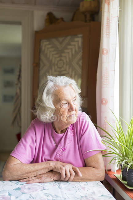 Seniorin blickt durch Fenster — Stockfoto