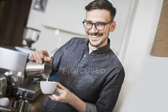 Sorridente barista fare il latte e guardando la fotocamera — Foto stock