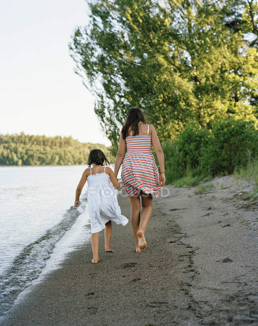 Rear view of two barefoot girls walking by sea — Stock Photo