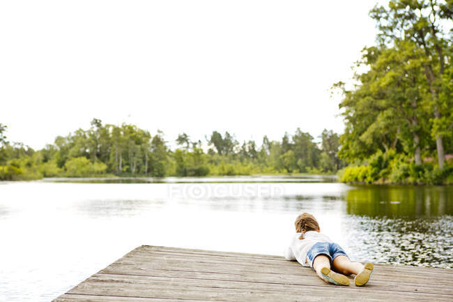 Ragazza sdraiata sul molo accanto al lago — Foto stock