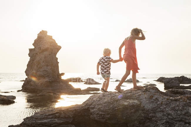 Ragazza che cammina con fratello sulle rocce costiere — Foto stock