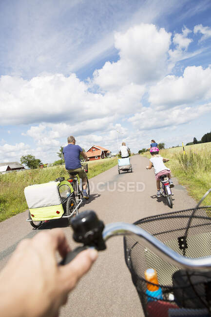 Family cycling on bicycles on rural road, back view — Stock Photo