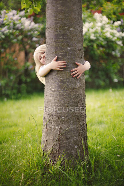 Girl with blonde hair hiding behind tree — Stock Photo