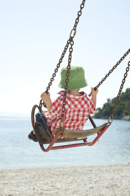 Garçon en chapeau de soleil vert assis sur swing — Photo de stock