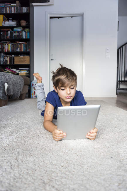 Мальчик лежит на полу с планшетным компьютером — стоковое фото