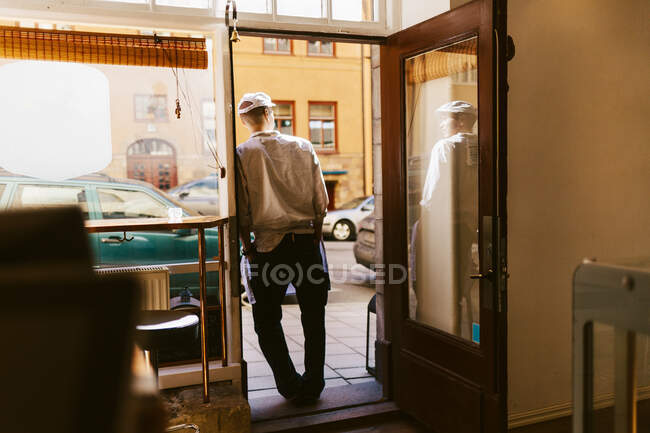 Vista posteriore del macellaio appoggiato sulla porta del negozio — Foto stock