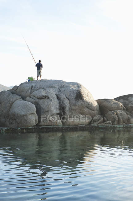 Hombre pescando en roca en Camps Bay en Ciudad del Cabo - foto de stock