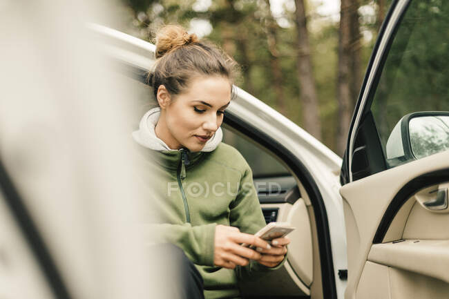 Giovane donna seduta in auto e con smartphone — Foto stock