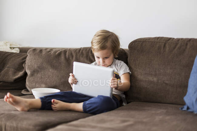 Мальчик на диване играет с планшетным компьютером — стоковое фото