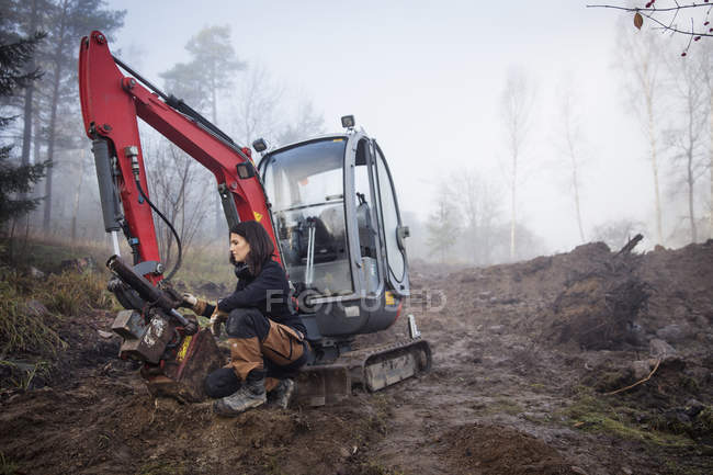 Young female worker crouching by earth mover in fog — Stock Photo