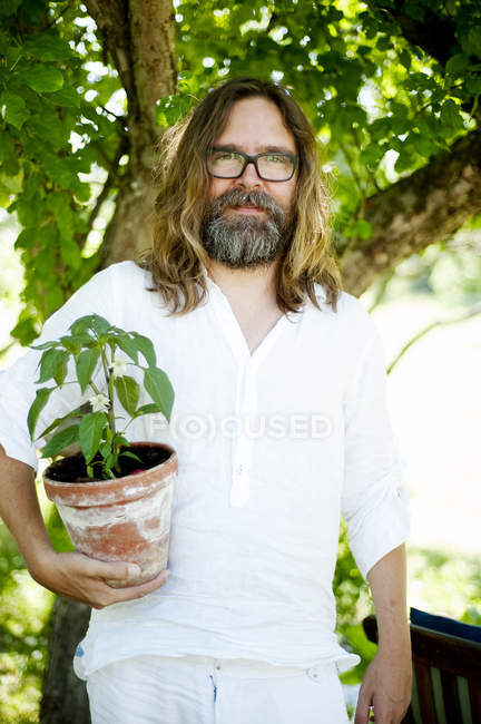 Homme debout avec une plante en pot regardant la caméra — Photo de stock