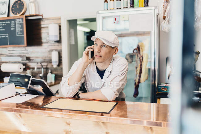 Boucher parlant au téléphone à la boucherie — Photo de stock