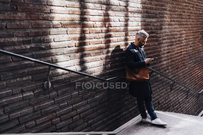 Man beside brick wall on smart phone — Stock Photo