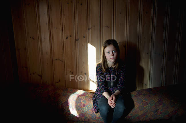 Teenage girl sitting against wooden wall — Stock Photo