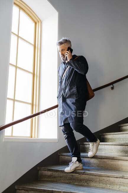Man talking on smart phone and walking down staircase — Stock Photo