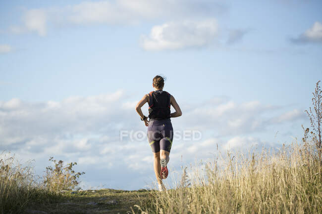 Donna jogging attraverso il campo, vista posteriore — Foto stock