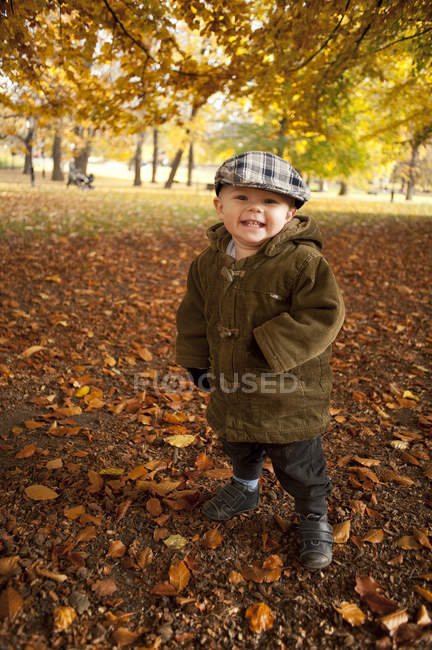 Portrait of boy standing in park at autumn, focus on foreground — Stock Photo