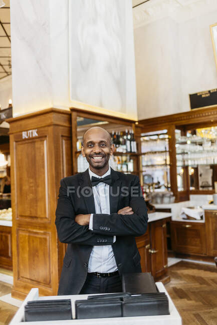 Waiter at bakery standing with crossed arms and smiling at camera — Stock Photo