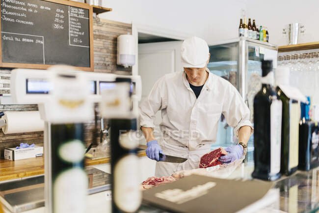 Мясник, нарезающий мясо в мясной лавке — стоковое фото