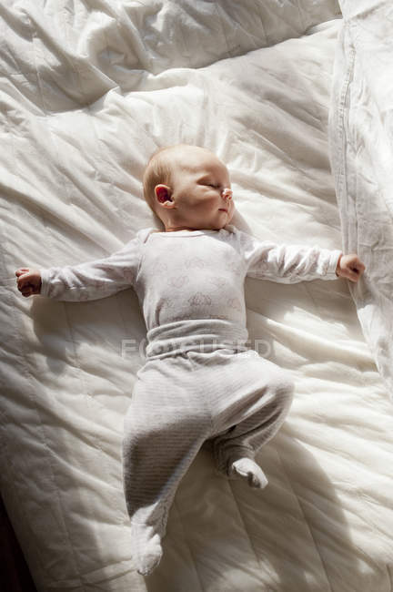 Baby girl lying down on white duvet — Stock Photo