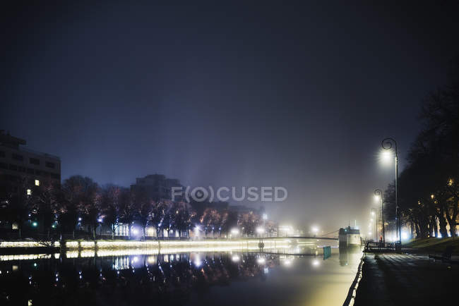Beleuchtetes Flussufer in der Nacht, Gebäude außen im Hintergrund — Stockfoto