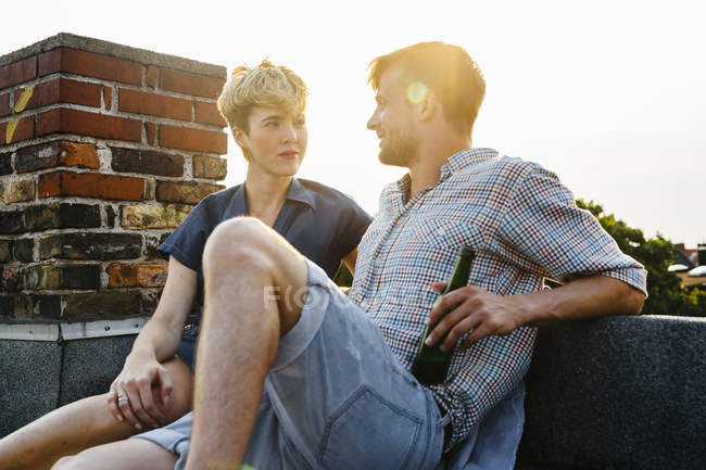 Молода пара сидить на даху з пивом в м'якому світлі — стокове фото