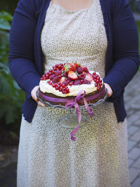 Femme portant un gâteau garni de baies fraîches — Photo de stock