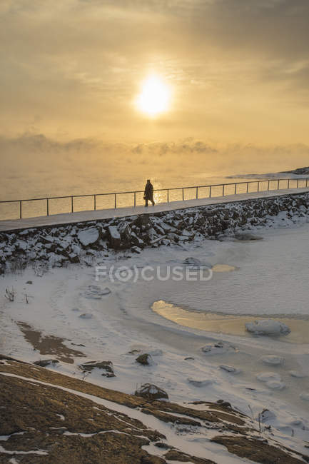 Silhouette of man walking on groyne at sunset — Stock Photo
