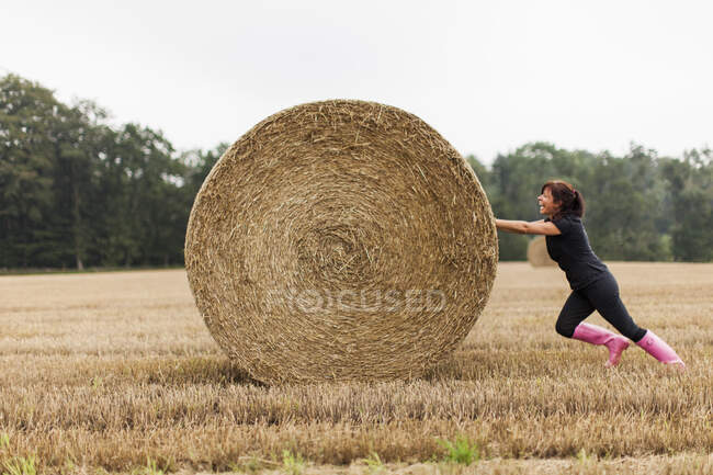 Woman pushing straw bale in field — Stock Photo