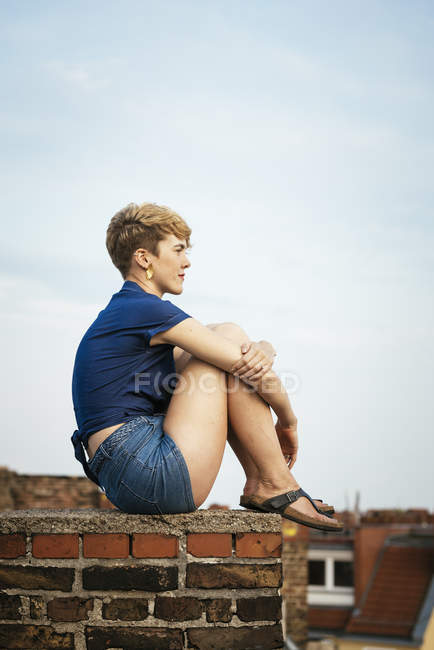 Junge blonde Frau sitzt bei Sonnenuntergang auf dem Dach, Seitenansicht — Stockfoto