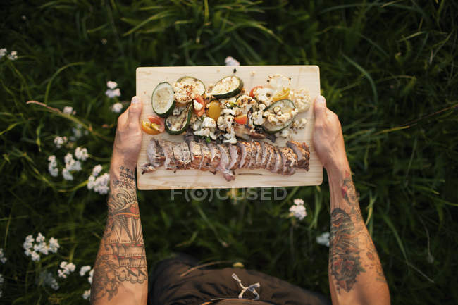 Чоловік тримає обробну дошку з м'ясом та овочами — стокове фото