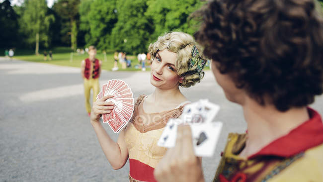 Young circus performers holding playing cards in park — Stock Photo