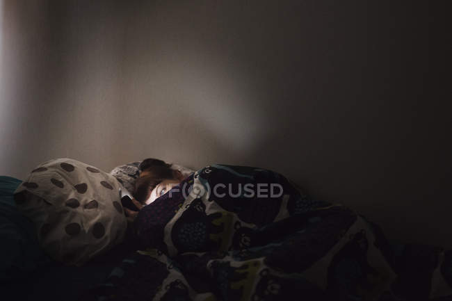 Jeune femme couchée au lit et utilisant le téléphone — Photo de stock
