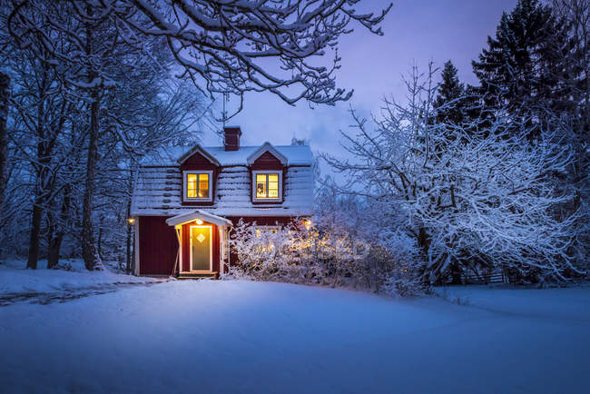 Casa de madera roja en la nieve al atardecer - foto de stock