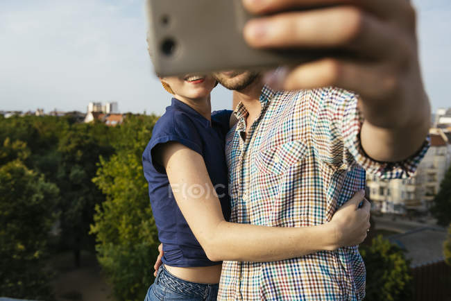 Young couple hugging and taking selfie with smartphone on town rooftop — Stock Photo