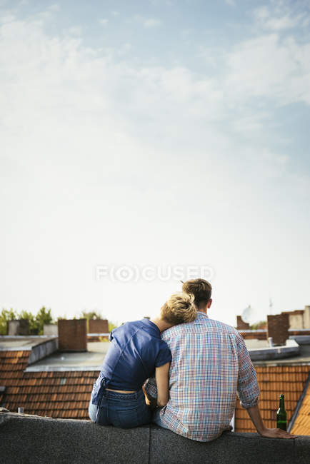 Вид сзади на молодую пару, сидящую на крыше вместе — стоковое фото