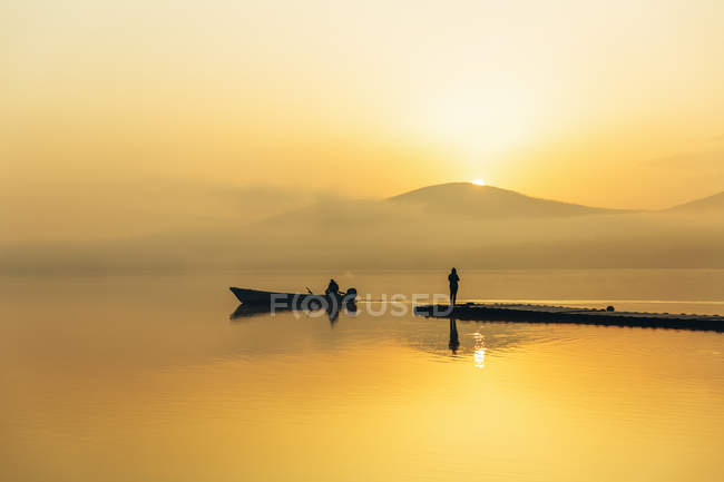 Silhouettes of two people in boat and on jetty — Stock Photo