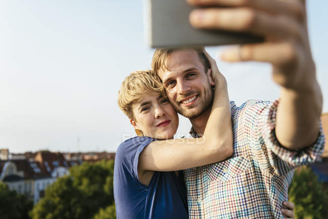 Молода пара обіймає і приймає селфі зі смартфоном на даху міста — стокове фото