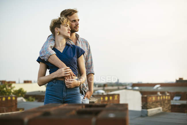 Giovane coppia abbracciare mentre in piedi sul tetto — Foto stock