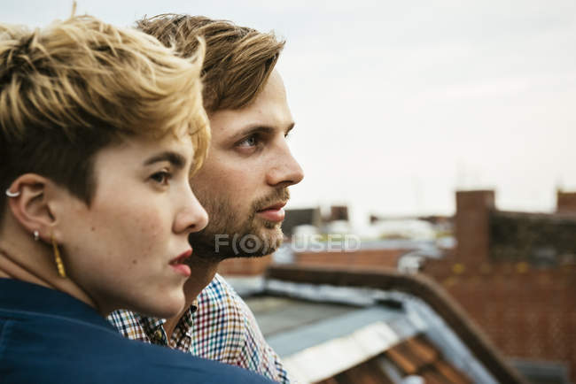 Jeune couple côte à côte sur le toit contre le ciel — Photo de stock