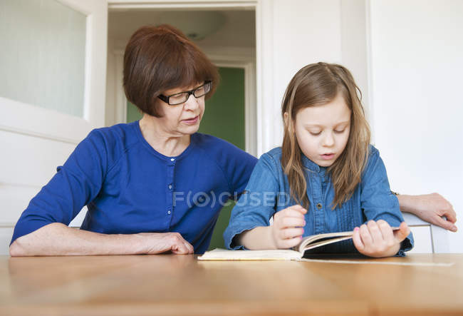 Porträt der Großmutter, die Enkelin bei den Hausaufgaben hilft, Fokus auf den Vordergrund — Stockfoto