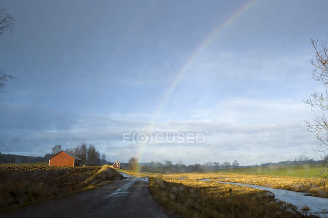 Arco iris sobre el paisaje rural con cabañas rojas falu y bosque distante - foto de stock