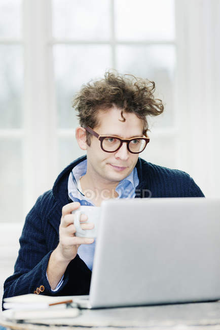 Homem usando laptop e segurando copo na mão — Fotografia de Stock